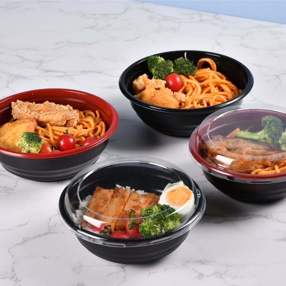 2 red and 2 black disposable plastic bowls, both filled with noodles and vegetables. One black and one red and black are covered with lids, while the other two are not covered with lids.