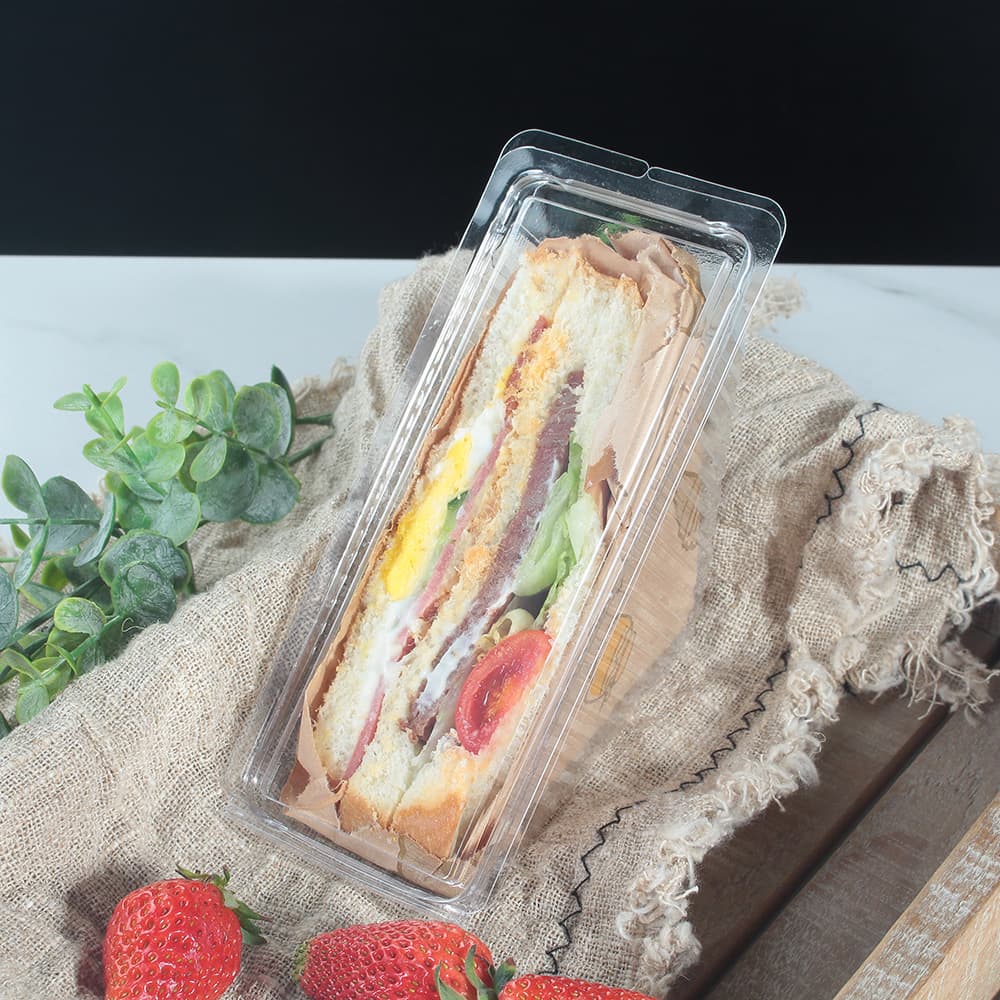 A clear clamshell container with sandwiches placed on a cloth strip inside a wooden board