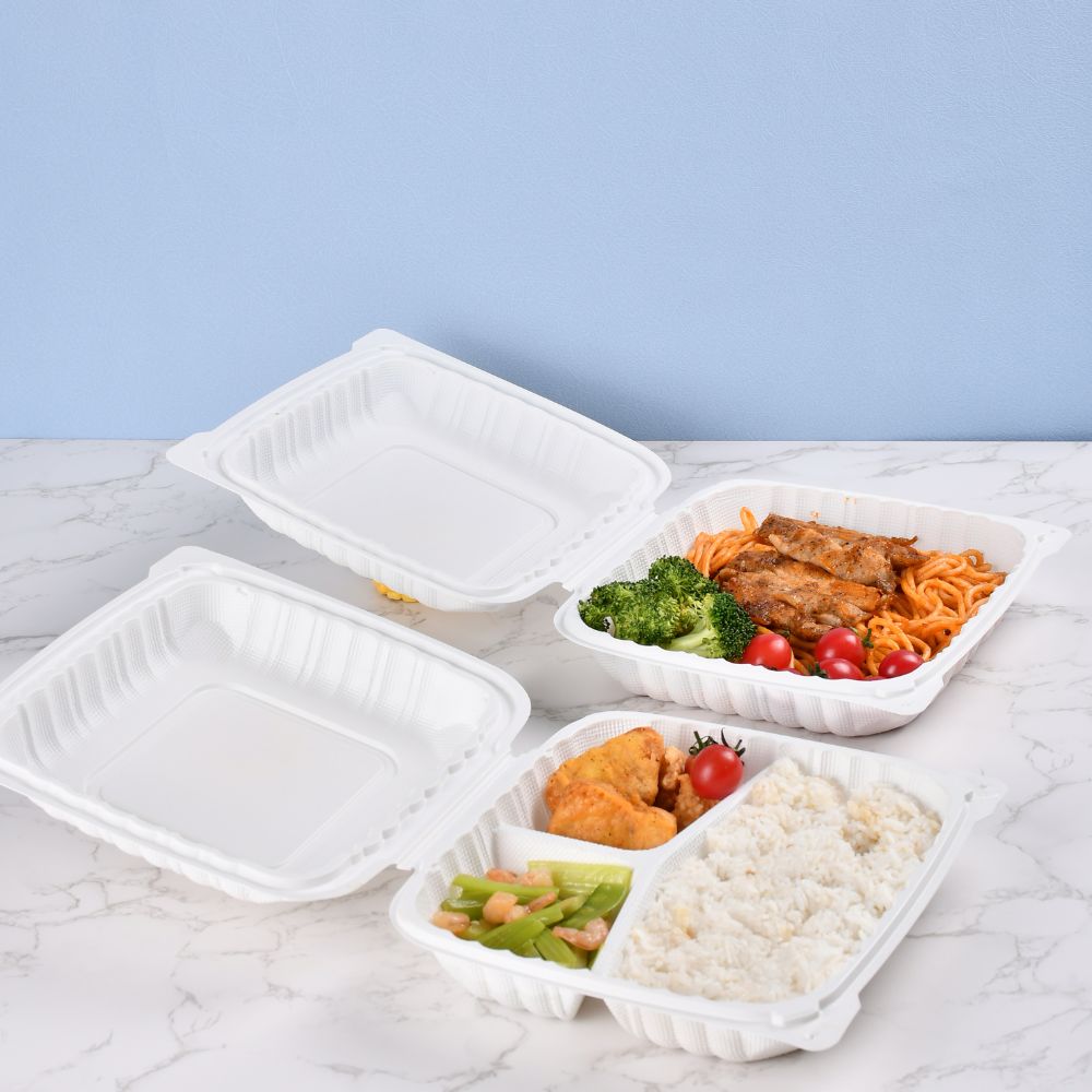 An undivided clamshell bento box containing broccoli, cherry tomatoes, chicken and noodles is placed on the table along with a clamshell bento box containing chicken nuggets, vegetables and rice.