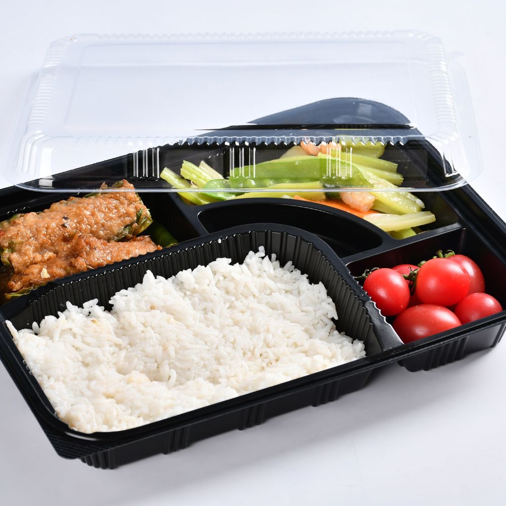 A black 5-compartment bento box with open lid containing vegetables, fruits and rice is placed on the table