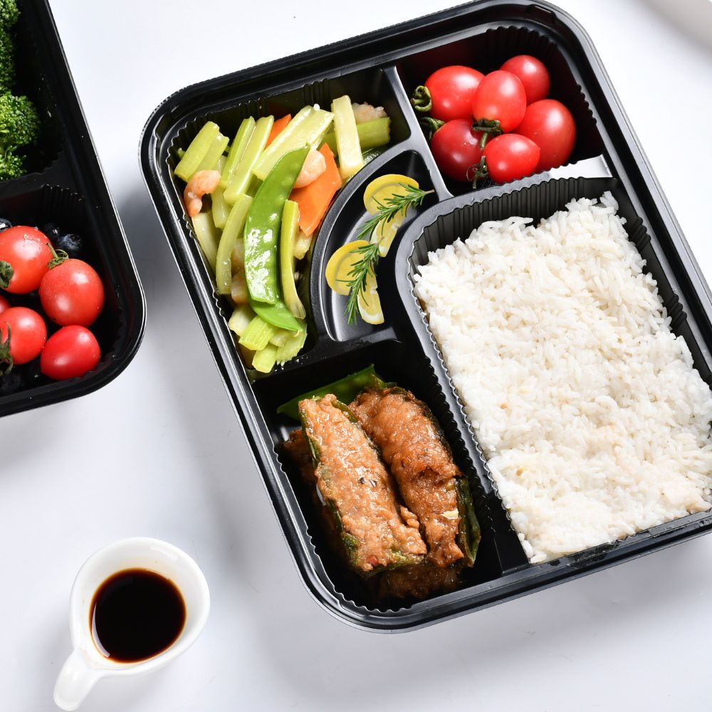An overhead shot of a black 5-part bento box containing food on the table