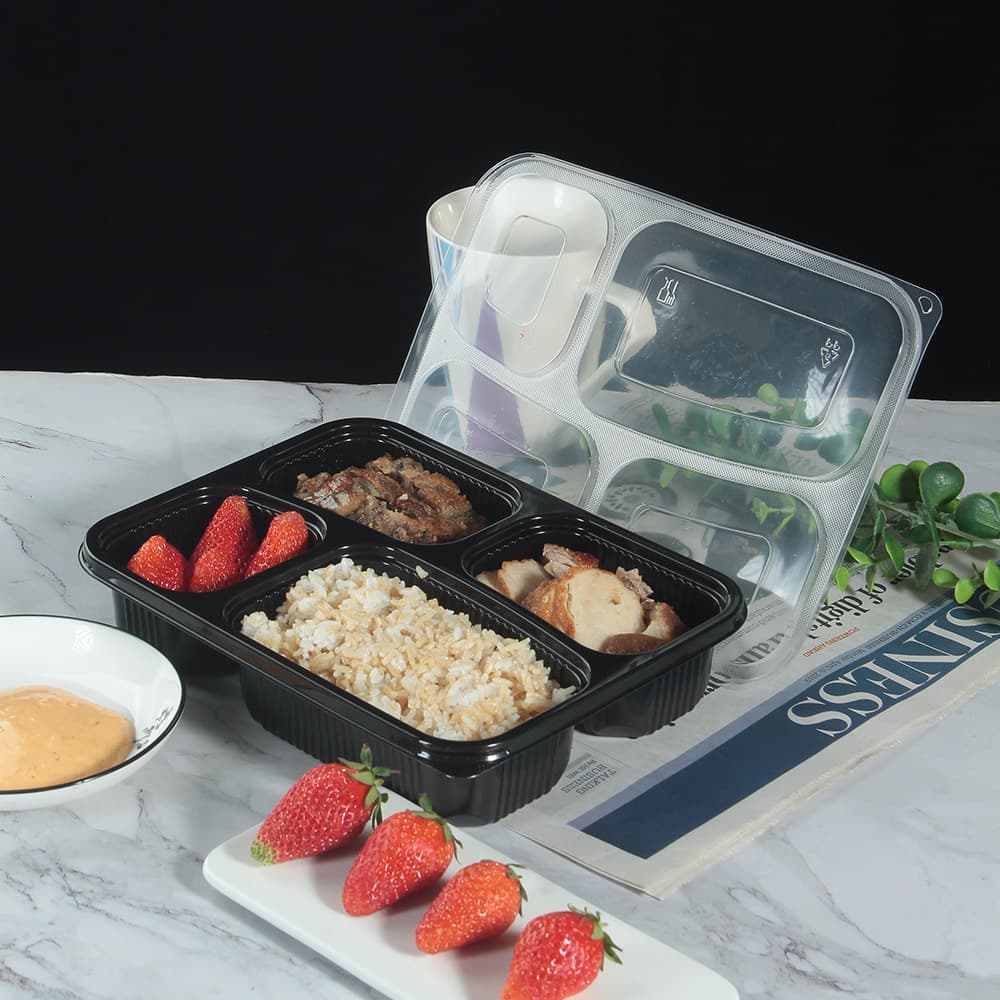 A 4-compartment lunch box with food and the lid open is placed on the table