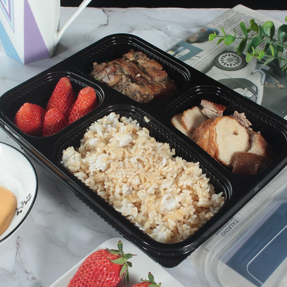 A 4-compartment lunch box with food and no lid is placed on the table