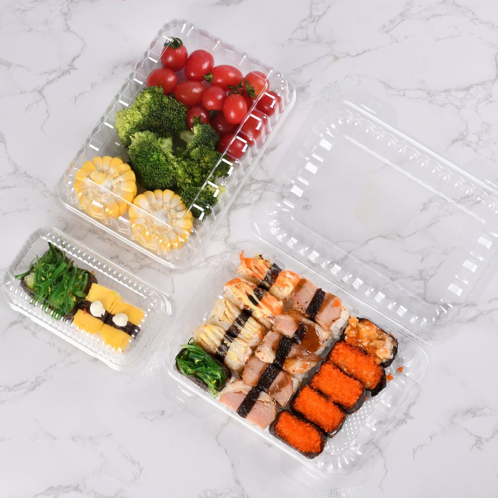 Three clear clamshell boxes of different sizes contain sushi, broccoli, corn, and cherry tomatoes respectively. Two of them have the lids closed, and one has the lid open.