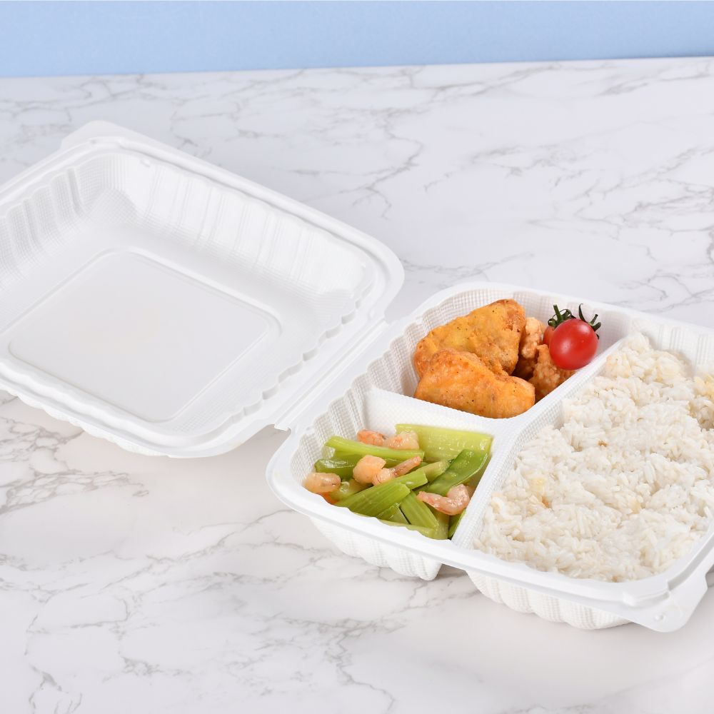 A 3-compartment disposable plastic clamshell bento box filled with chicken nuggets, vegetables and rice is placed on the table