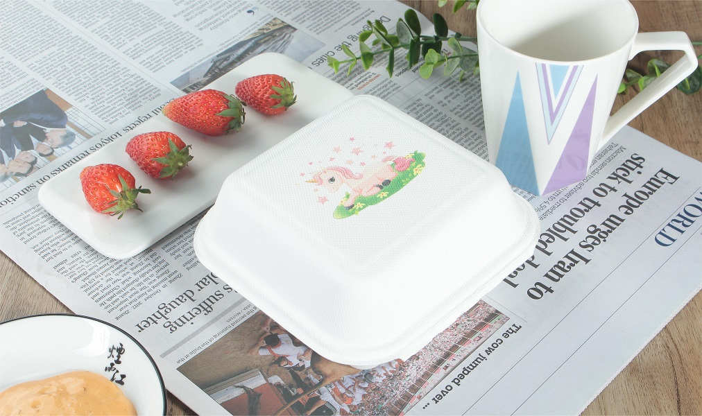 A white expedited bagasse Clamshell Container with a pink pony logo is placed on a table covered with newspapers, with strawberries and cups as decorations next to it.