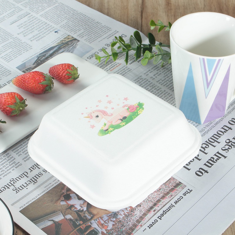 A clamshell container with a closed lid and a pink pony logo printed on it, placed on a table covered with newspapers, with some strawberries and a cup on the table